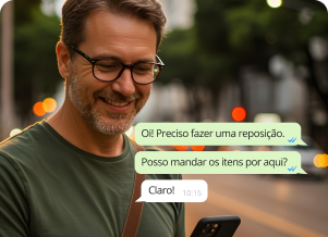 Homem de óculos sorrindo e olhando para o celular, feliz por atender o cliente com as soluções com IA da Mercos. Ao seu lado aparece, com zoom na tela, a conversa que ele está tendo com um cliente, que envia: "Oi! Preciso fazer uma reposição. Posso mandar os itens aqui?". Ele responde "Claro!".